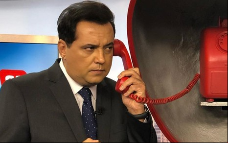 Geraldo Luís segurando o telefone de um orelhão instalado no cenário do Balanço Geral SP