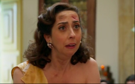 Com arranhões no rosto, a atriz Marinna Armellini faz expressão de surpresa caracterizada como Clarice em cena de Êta Mundo Bom!