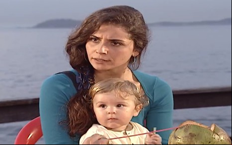 A Atriz Giovanna Antonelli, com um bebê no colo e expressão de desagrado, em cena como Capitu em Laços de Família