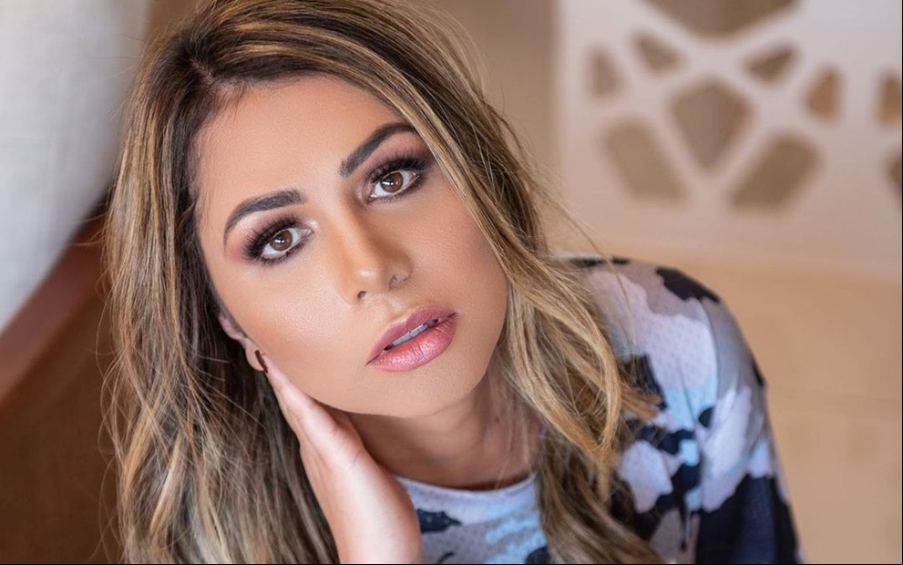 Mallu Ohana de camiseta estampada, com a mão no rosto e cabelo solto com cachos