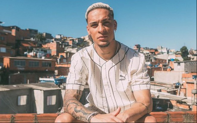 Antony sentado em frente à uma comunidade com cara séria
