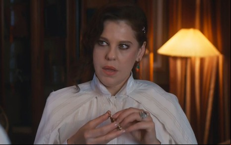 Barbara Paz está caracterizada como sua personagem de Além da Ilusão, novela das seis da Globo; ela olha para o lado e usa blusa clara