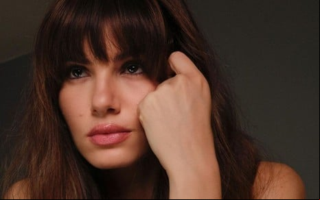 De franja, Camila Queiroz com cara de cansada olha para o lado e apoia o rosto sobre as mãos