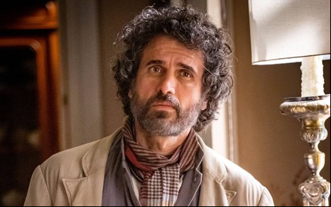 Eriberto Leão em foto de divulgação de Além da Ilusão: ele está com o cabelo na nuca, branca, terno branco surrado e olha para frente