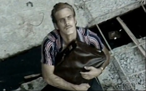 Francisco Cuoco segura uma mala e olha para cima em cena como Carlão da novela Pecado Capital (1975)