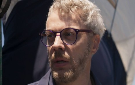 Ator Guilherme Weber olha para frente com cara de sério em cena de Cara e Coragem
