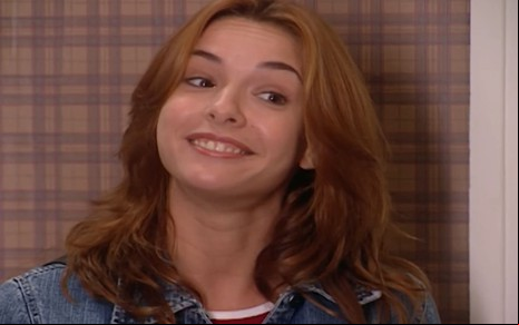 Regiane Alves caracterizada como Dóris; ela usa uma blusa rosa e tem os cabelos médios e ruivos. O semblante exprime deboche em cena de Mulheres Apaixonadas.