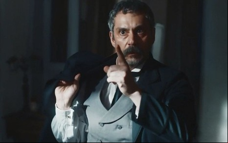 O ator Alexandre Nero com o dedo indicador da mão direita em riste como o Tonico em cena de Nos Tempos do Imperador