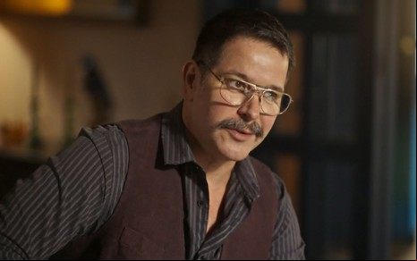 Tenório (Murilo Benício) está sentado em escritório e usa óculos em cena de Pantanal, novela das nove da Globo