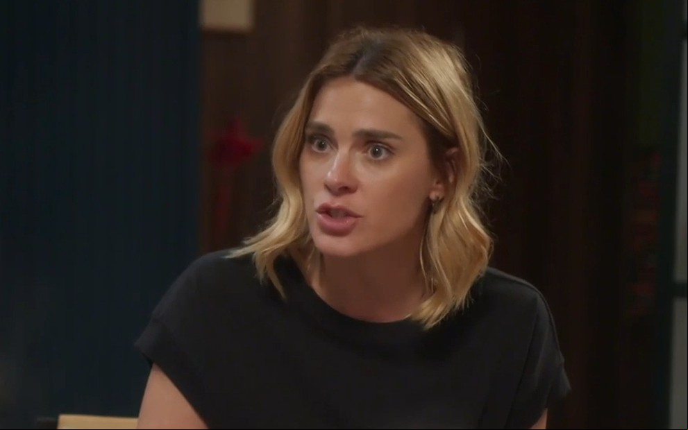 Carolina Dieckmann caracterizada como Lumiar; ela tem os cabelos loiros e curtos e veste roupa social. O semblante está sério em cena de Vai na Fé.
