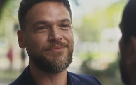 Emilio Dantas caracterizado como Theo em Vai na Fé; ele usa um terno azul escuro e dá um sorriso debochado