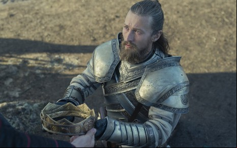 Elliott Tittensor veste traje de cavaleiro e exibe coroa em cena de House of the Dragon