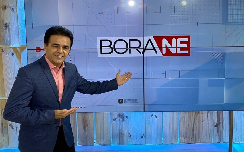 Herbeth de Souza com um terno azul e uma blusa rosa, mostrando o logotipo do Bora Nordeste