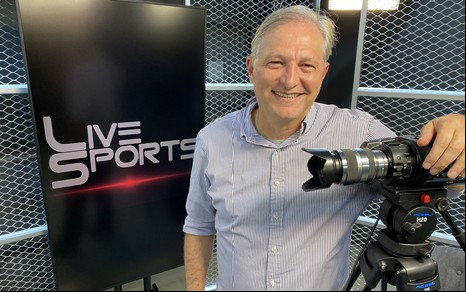 João Palomino com uma camisa listrada e sorrindo para uma foto nos estúdios de sua produtora