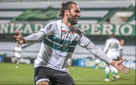 Léo Gamalho comemora gol do Coritiba na Série B. Ele usa uma camisa branca com faixas verdes.