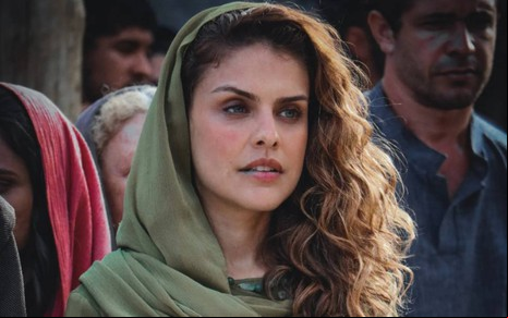 A atriz Paloma Bernardi com expressão séria, lenço na cabeça, em cena da novela Reis