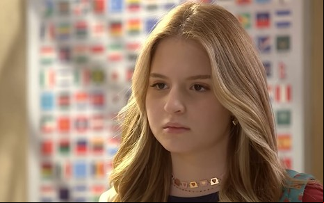 A atriz Sophia Valverde como Poliana em Poliana Moça; ela está de lado, olhando para frente com cara séria