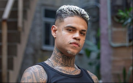 O ator MC Cabelinho caracterizado como o personagem Hugo em Vai na Fé, olha para a câmera