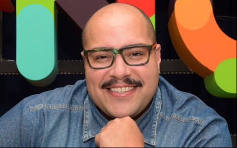Tiago Abravanel sorri, com a mão apoiada no queixo