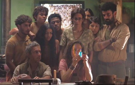 Zefa Leonel (Andrea Beltão) segura pedra preciosa azul na mão; toda a família está em volta dela na cena da novela No Rancho Fundo
