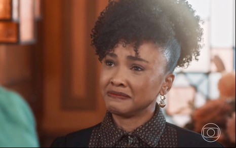 Kênia Bárbara chora em cena da novela Amor Perfeito como a personagem Lucília; ela está com cabelo preso e camisa estampada