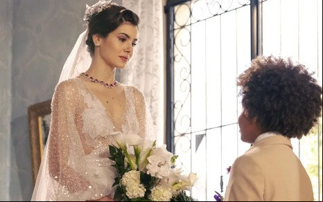 Camila Queiroz caracterizada como Marê; ela está com os cabelos amarrados em um coque e usa um vestido de noiva. O semblante exprime alegria em cena de Amor Perfeito.