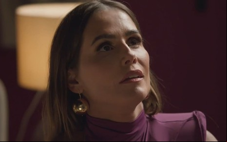 Deborah Secco caracterizada como Lara; ela usa uma blusa rosa e está espantada em cena de Elas por Elas