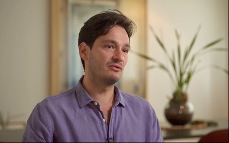 O autor Bruno Luperi está sentado, usa camisa lilás e dá entrevista sobre Renascer ao programa Fantástico
