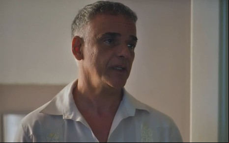 Ângelo Antônio caracterizado como Andrade; ele usa uma camisa branca e parece tenso em cena de Terra e Paixão