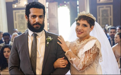 De terno, Amaury Lorenzo dá o braço para Diego Martins, que está com vestido de noiva, segurar em cena de Terra e Paixão
