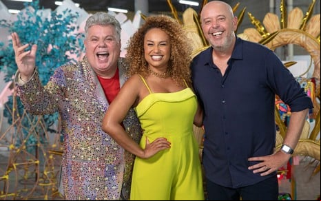 Milton Cunha, Karine Xavier e Alex Escobar à frente de objetos de desfile de escolas de samba em foto de divulgação das transmissões de 2024
