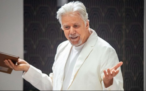 Reginaldo Faria usa terno branco e está com os braços abertos