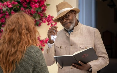 Samuel L. Jackson faz um aceno de cabeça com a mão em um chapéu, para uma mulher ruiva que está de costas para a câmera
