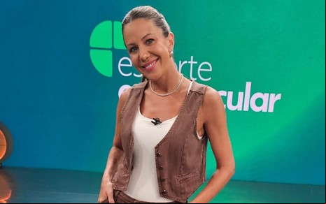 Bárbara Coelho usa uma regata branca com colete marrom por cima e está com cabelo preso; ao fundo está o logo do Esporte Espetacular no telão