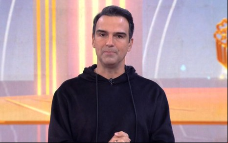 Tadeu Schmidt usa uma blusa preta enquanto apresenta o BBB 25, que entra no ar em outro horário hoje (20)