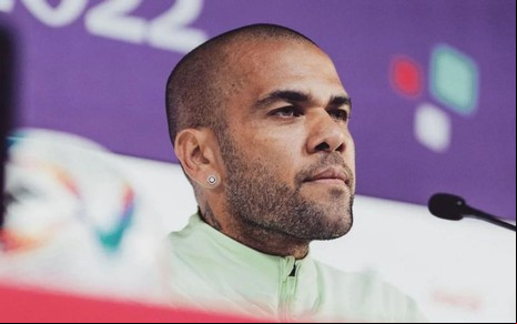 Daniel Alves sentado em mesa de coletiva de imprensa, com feição séria
