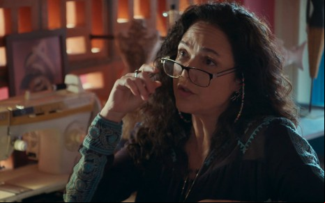 A atriz Tereza Seiblitz com dedo segurando óculos no rosto, expressão séria, em cena de Volta por Cima