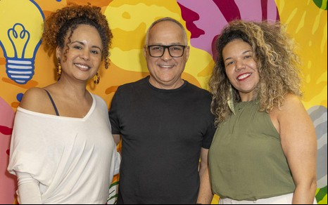 Renata Andrade, Amauri Soares e Thais Pontes posam sorridentes para foto em um backdrop colorido