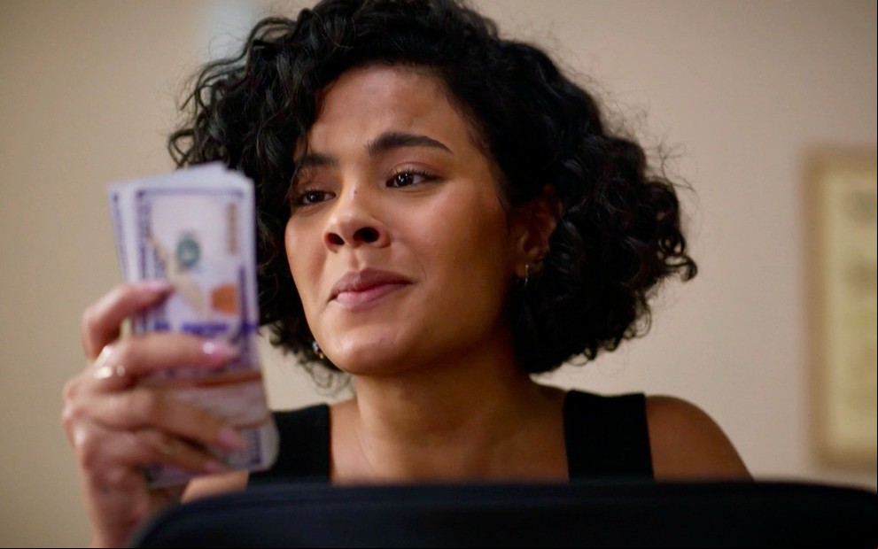 Bella Campos como Maria de Fátima segura maço de dólares no remake de Vale Tudo, da Globo