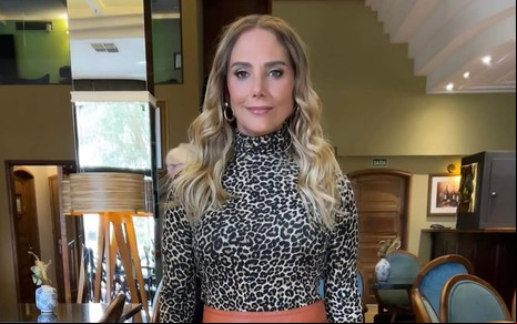 Heloisa Périssé usa um body de animal print e está com os cabelos loiros soltos; ela dá um leve sorriso para a câmera