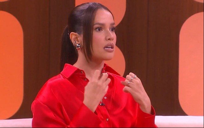 Juliette Freire em sua estreia no Saia Justa; ela está sentada no sofá, de camisa vermelha, com expressão de medo
