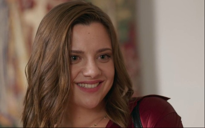 Manu Morelli com expressão sorridente como Carol em cena da novela Beleza Fatal