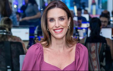 Paula Monteiro sorri, com uma redação jornalística no fundo da imagem