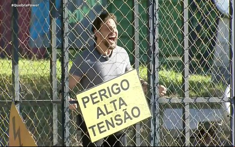 Rafael Pessina está dentro de uma gaiola com uma placa de "Perigo: Alta Tensão" na grade
