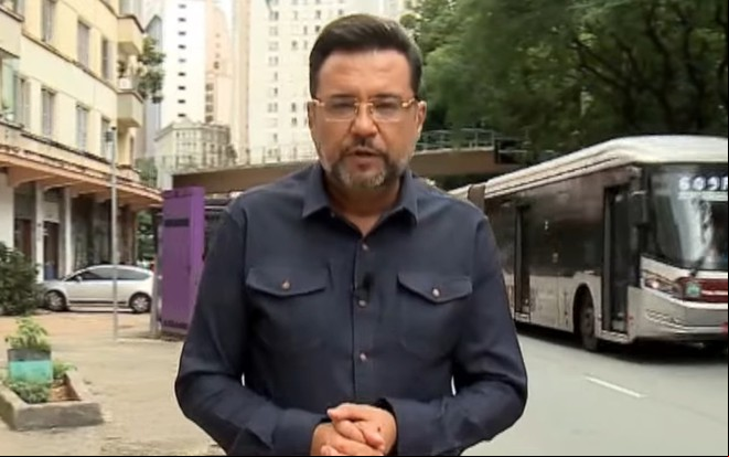 Geraldo Luís está numa calçada, com um ônibus ando ao fundo; ele tem expressão séria