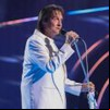 Roberto Carlos cantando em um palco à frente de um microfone; ele está de perfil