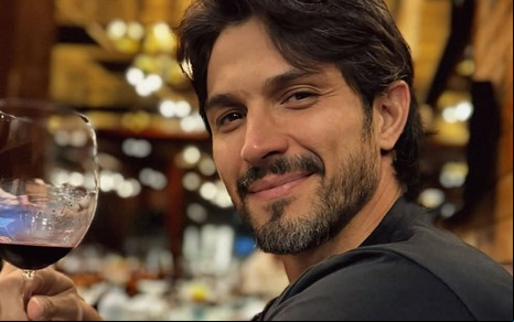 Romulo Estrela posando com sorriso leve, segurando uma taça de vinho