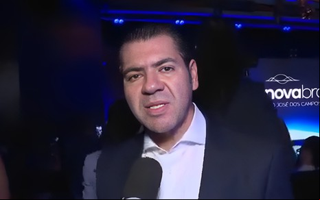 Daniel Abravanel fala em microfone e olha para a câmera com expressão de contragosto
