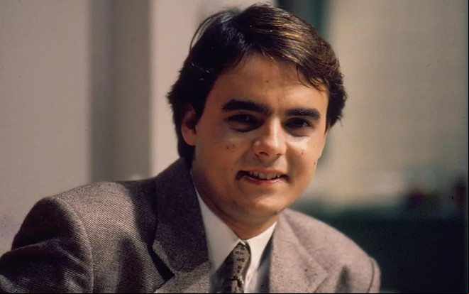 O ator Cassio Gabus Mendes sorrindo de terno e gravata, caracterizado como Afonso em Vale Tudo (1988)